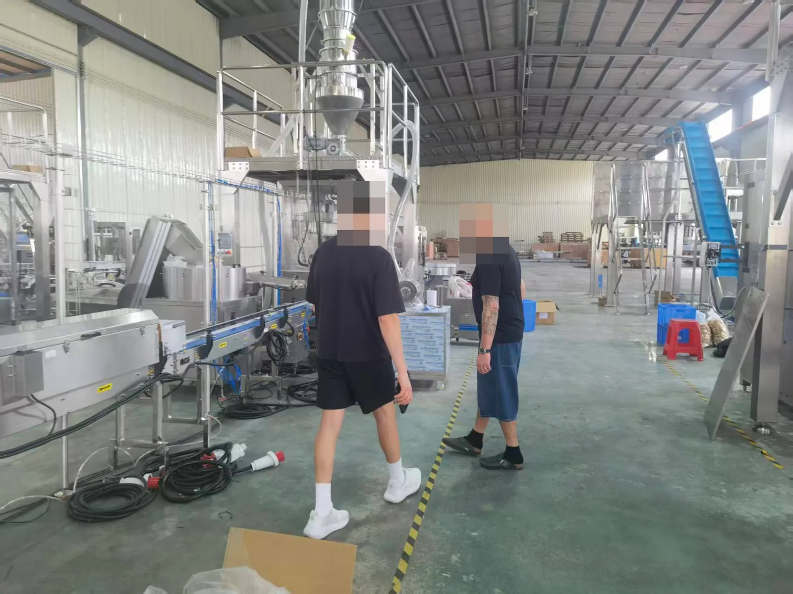 Packaging machinery on a production floor; people anonymised.